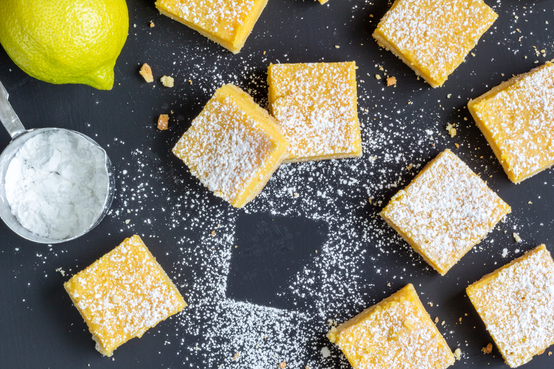 honey buttered lemon squares on a dark backdrop with powdered sugar sprinkled on top